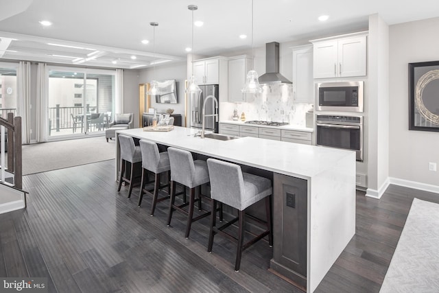 kitchen with pendant lighting, white cabinets, wall chimney range hood, sink, and appliances with stainless steel finishes