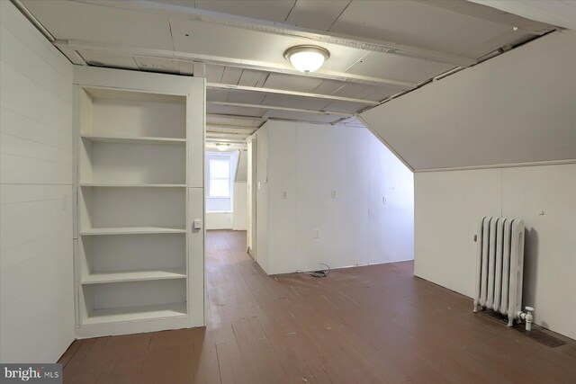 additional living space with built in shelves, lofted ceiling, hardwood / wood-style flooring, and radiator