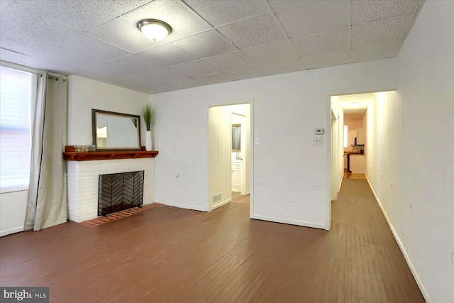 unfurnished living room featuring a paneled ceiling, a brick fireplace, and hardwood / wood-style floors