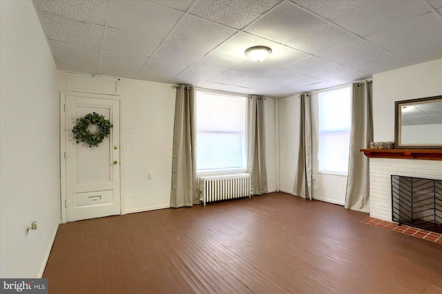 unfurnished living room with dark hardwood / wood-style flooring, a brick fireplace, and radiator