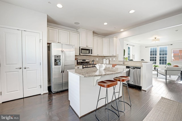 kitchen with backsplash, kitchen peninsula, a breakfast bar area, white cabinets, and appliances with stainless steel finishes