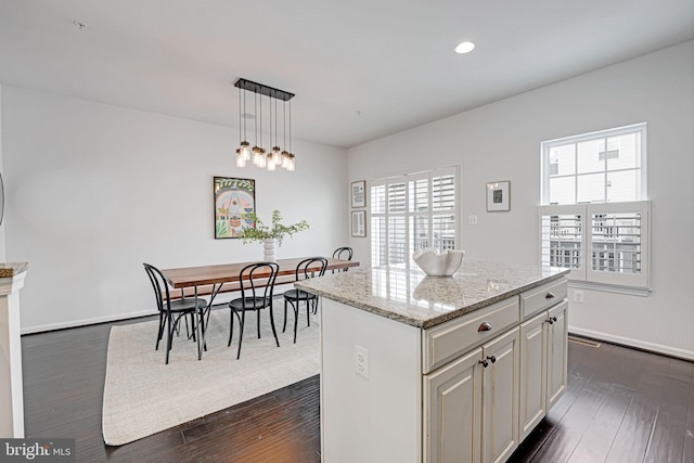 kitchen featuring light stone countertops, a center island, decorative light fixtures, and a healthy amount of sunlight