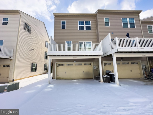 snow covered house featuring cooling unit and a garage