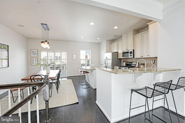 kitchen with stainless steel appliances, light stone counters, kitchen peninsula, decorative light fixtures, and decorative backsplash