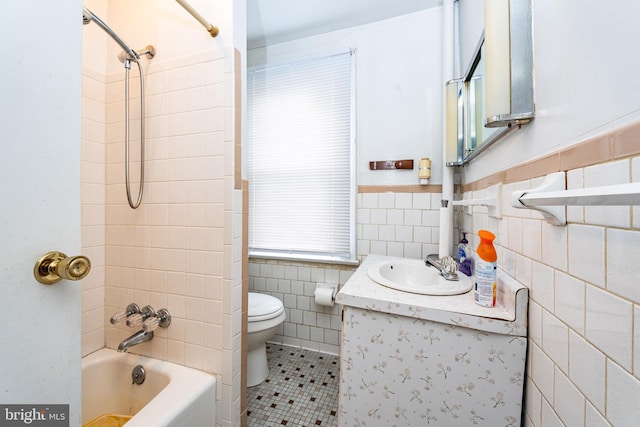 full bathroom with tile patterned floors, vanity, tiled shower / bath combo, tile walls, and toilet