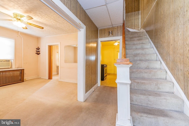 stairs featuring cooling unit, radiator, wooden walls, and carpet