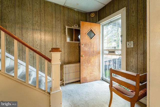 interior space with carpet flooring, wooden walls, a drop ceiling, and radiator