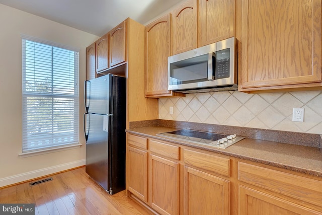 kitchen featuring cooktop, backsplash, light brown cabinets, and black refrigerator