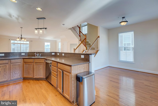 kitchen with a notable chandelier, stainless steel dishwasher, sink, light hardwood / wood-style flooring, and hanging light fixtures