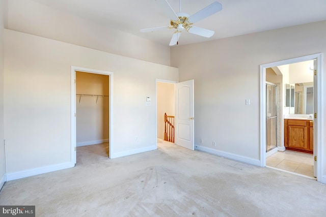 unfurnished bedroom featuring ceiling fan, connected bathroom, a closet, light colored carpet, and a walk in closet