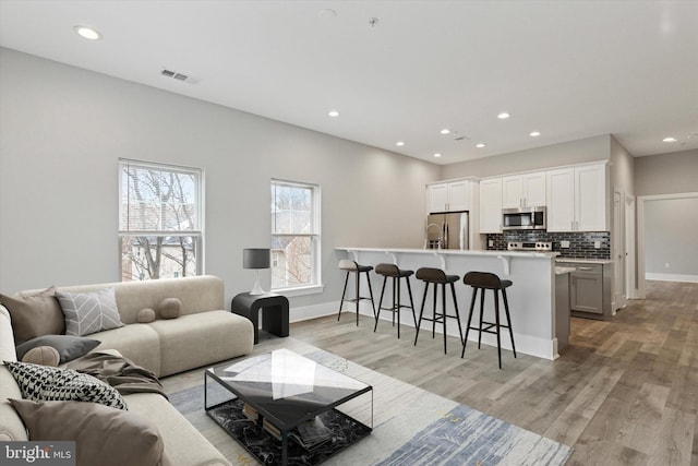 living area with light wood-type flooring, visible vents, and recessed lighting