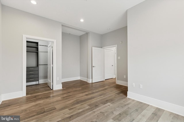 unfurnished bedroom with recessed lighting, a walk in closet, baseboards, and wood finished floors