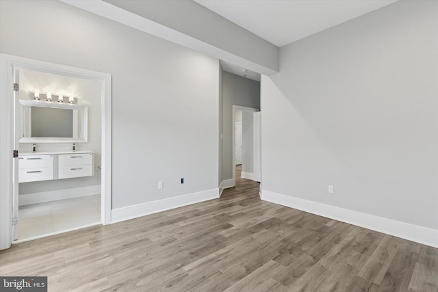 unfurnished bedroom with light wood-style flooring, baseboards, and connected bathroom