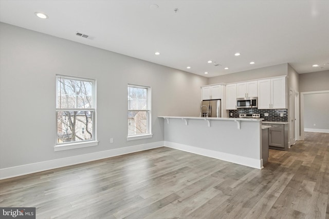 kitchen featuring a peninsula, visible vents, a kitchen breakfast bar, appliances with stainless steel finishes, and decorative backsplash