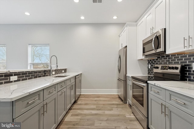 kitchen featuring gray cabinetry, appliances with stainless steel finishes, a sink, light wood-type flooring, and baseboards