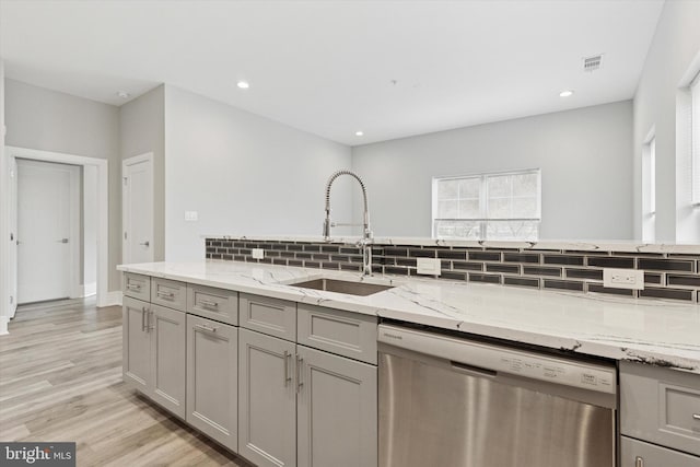 kitchen featuring light wood finished floors, tasteful backsplash, gray cabinetry, a sink, and dishwasher