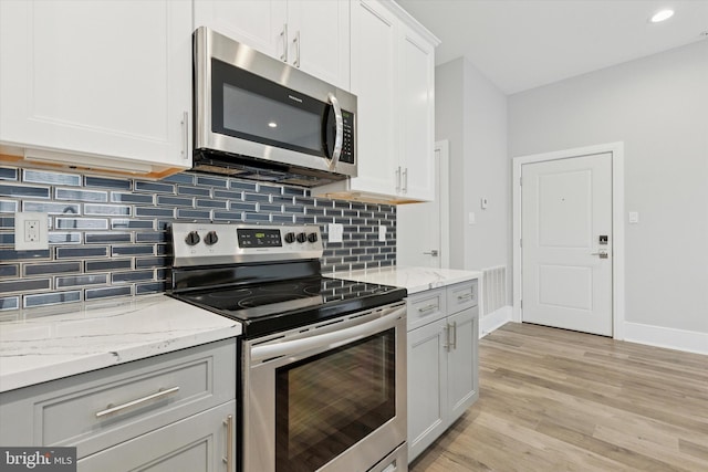 kitchen with backsplash, appliances with stainless steel finishes, light wood-style floors, white cabinets, and baseboards