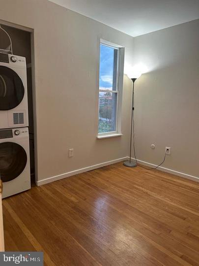 clothes washing area with stacked washer and dryer and hardwood / wood-style flooring