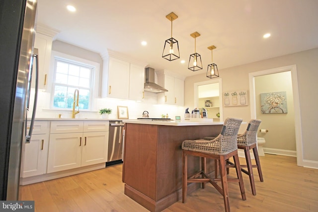 kitchen with decorative light fixtures, wall chimney range hood, stainless steel refrigerator, and white cabinetry