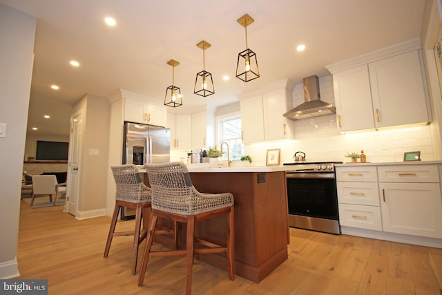 kitchen featuring stainless steel appliances, white cabinetry, wall chimney exhaust hood, pendant lighting, and a breakfast bar