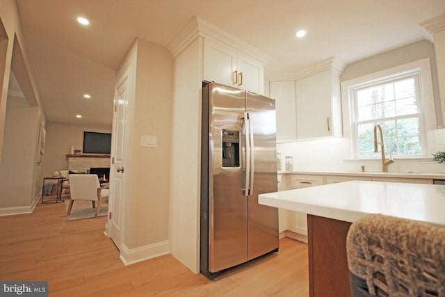 kitchen with white cabinets, light wood-type flooring, stainless steel fridge, and sink