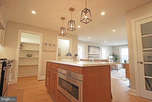 kitchen featuring decorative light fixtures, light wood-type flooring, appliances with stainless steel finishes, and a center island