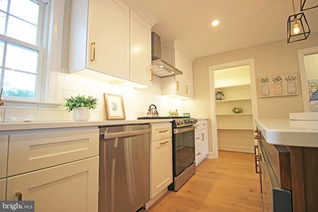 kitchen with light hardwood / wood-style flooring, pendant lighting, stainless steel appliances, wall chimney range hood, and white cabinets