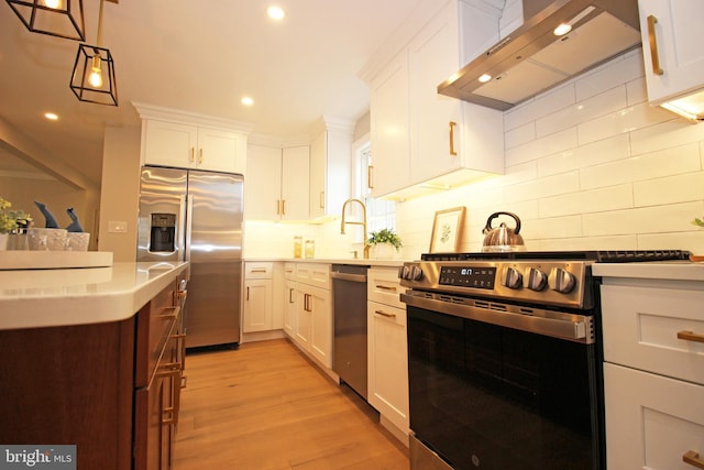 kitchen with appliances with stainless steel finishes, wall chimney exhaust hood, hanging light fixtures, and white cabinetry