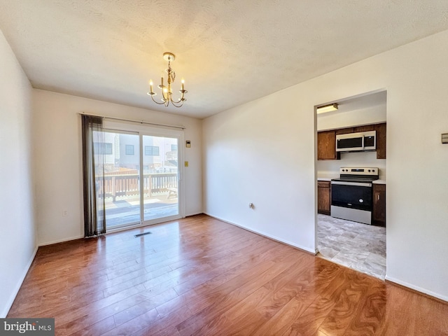 empty room featuring light wood-type flooring, a textured ceiling, and a chandelier