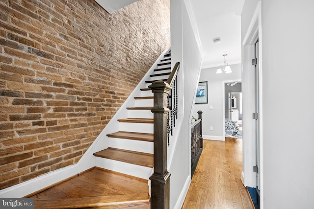 stairway with hardwood / wood-style floors, an inviting chandelier, and brick wall