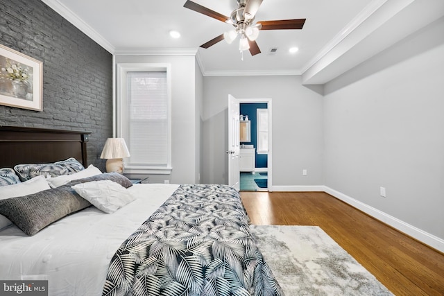 bedroom with connected bathroom, ceiling fan, a large fireplace, crown molding, and wood-type flooring