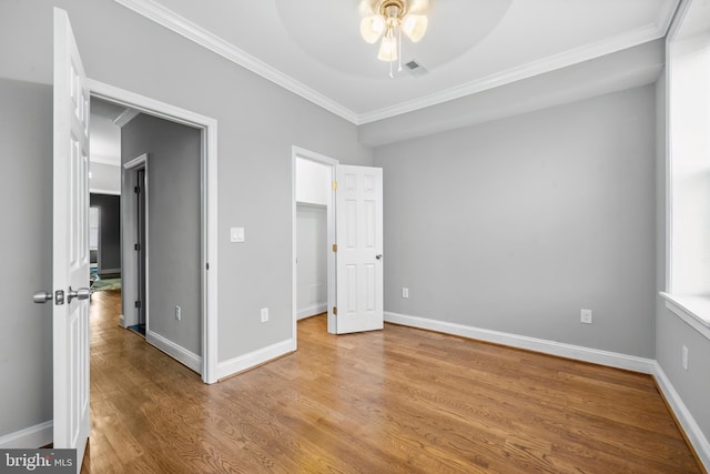 unfurnished bedroom with ceiling fan, a walk in closet, wood-type flooring, and crown molding