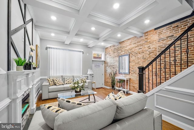 living room featuring coffered ceiling, light hardwood / wood-style flooring, beamed ceiling, brick wall, and a fireplace