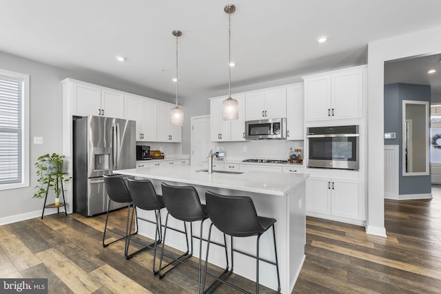 kitchen featuring hanging light fixtures, stainless steel appliances, a kitchen island with sink, white cabinets, and sink