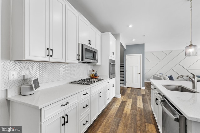 kitchen with stainless steel appliances, light stone counters, white cabinets, decorative light fixtures, and sink