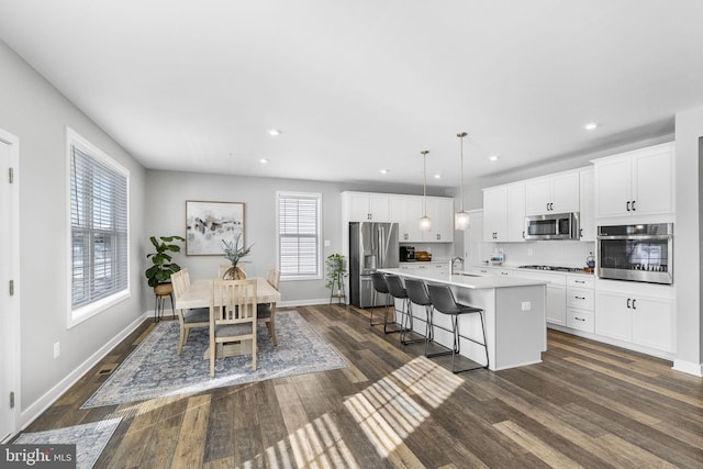 kitchen featuring a center island with sink, appliances with stainless steel finishes, hanging light fixtures, a kitchen bar, and white cabinets