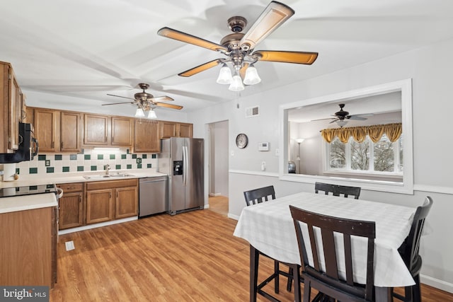 kitchen featuring ceiling fan, sink, backsplash, light hardwood / wood-style floors, and appliances with stainless steel finishes