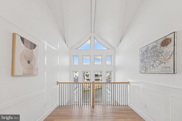 corridor with high vaulted ceiling and light hardwood / wood-style flooring