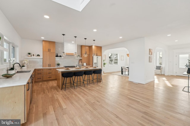 kitchen with high end refrigerator, sink, decorative light fixtures, light hardwood / wood-style floors, and a kitchen bar