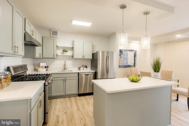 kitchen featuring backsplash, sink, hanging light fixtures, light wood-type flooring, and stainless steel appliances