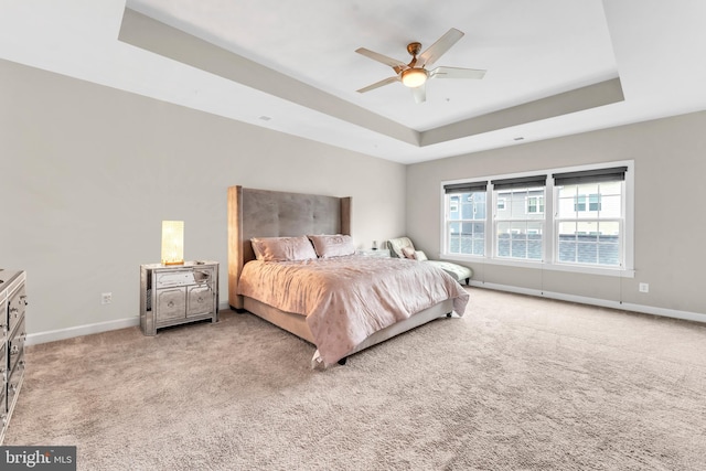 bedroom with light colored carpet, a raised ceiling, and ceiling fan