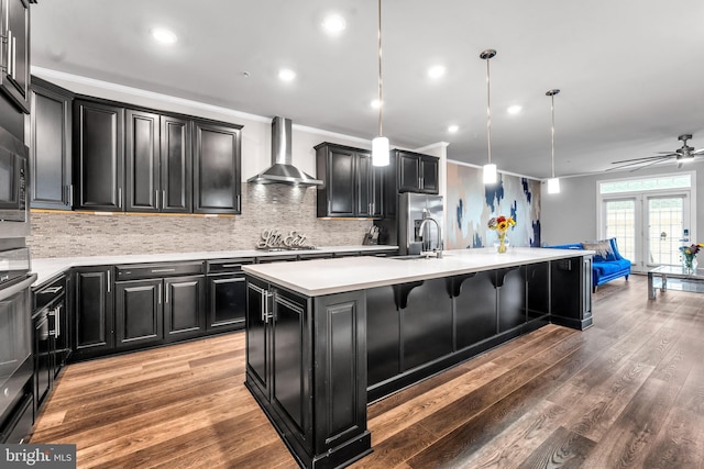 kitchen featuring sink, wall chimney exhaust hood, hardwood / wood-style floors, pendant lighting, and a kitchen island with sink