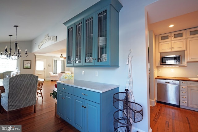 kitchen featuring dark wood-type flooring, appliances with stainless steel finishes, blue cabinets, and ceiling fan with notable chandelier