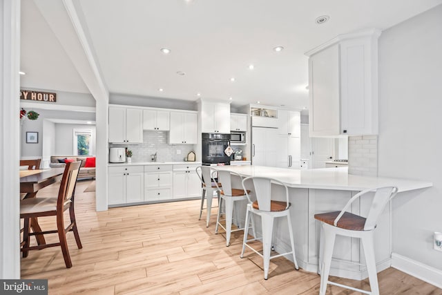 kitchen with backsplash, a kitchen breakfast bar, kitchen peninsula, built in appliances, and white cabinetry