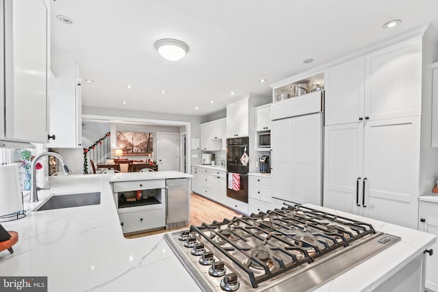 kitchen with white cabinets, light stone countertops, kitchen peninsula, and sink