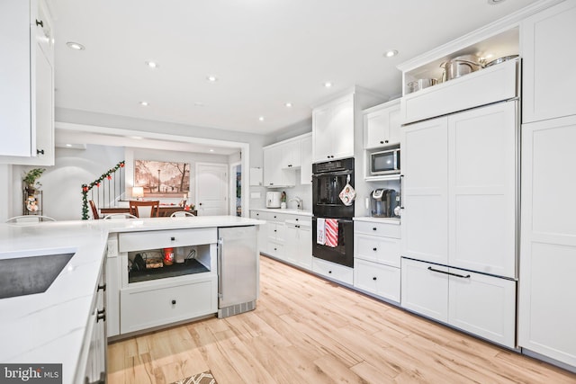 kitchen with white cabinets, light hardwood / wood-style flooring, light stone countertops, built in microwave, and double oven