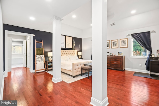 bedroom with wood-type flooring, ornate columns, and ensuite bath