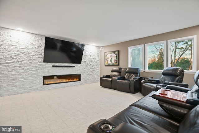 home theater room with a stone fireplace and light carpet