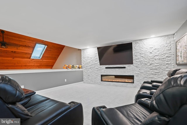 carpeted cinema room featuring a skylight and a stone fireplace