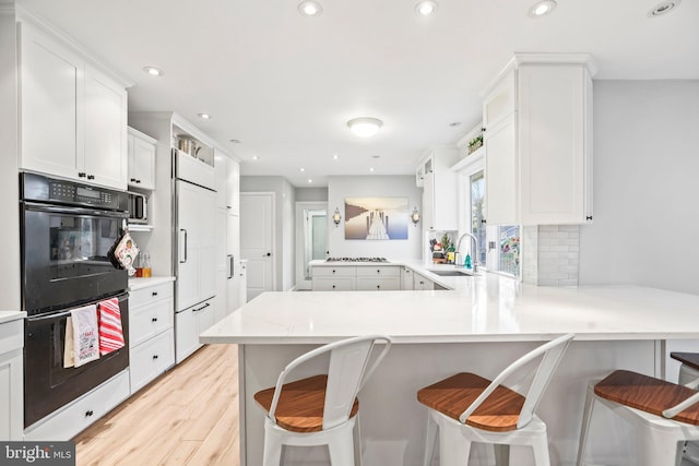 kitchen featuring white cabinetry, sink, a kitchen breakfast bar, kitchen peninsula, and black double oven